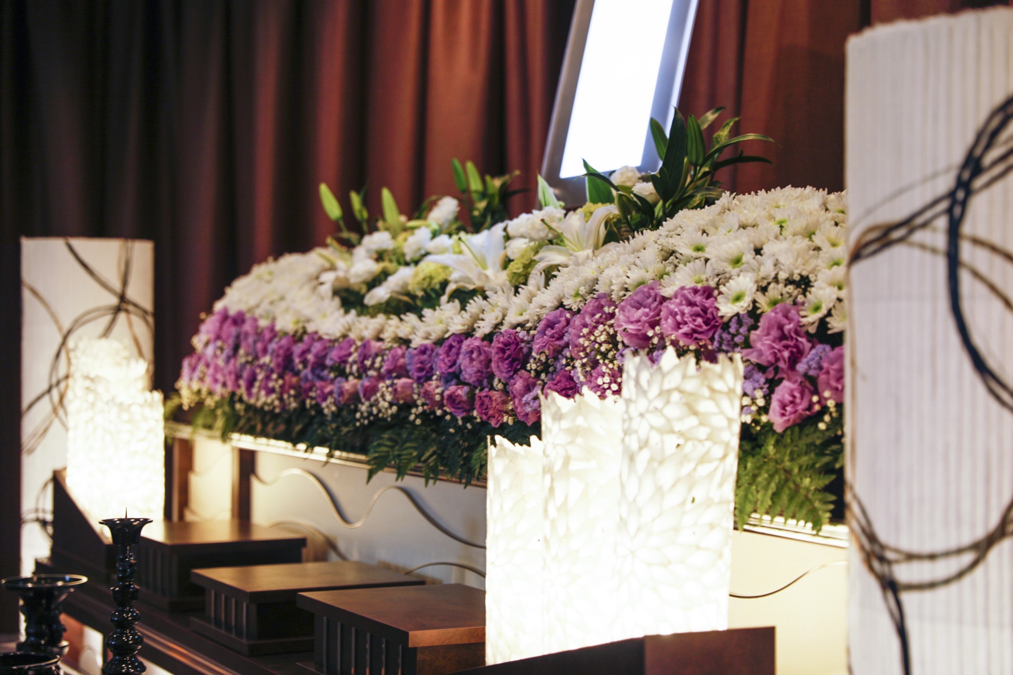 白菊と紫の花で組まれた生花祭壇。行灯の柔らかな灯りに照らされている